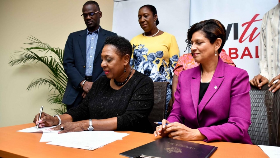 The Ministry of Culture, Gender, Entertainment and Sport, the Honourable Olivia Grange (left) signs the Memorandum of Understanding with the UWI Open Campus for sexual harassment training in workplaces.  The Pro-Vice Chancellor and Principal of the UWI Open Campus, Dr Luz Longsworth (seated right) as well as the Permanent Secretary in the Ministry, Denzil Thorpe (standing left) and the Senior Director of the Bureau of Gender Affairs, Sharon Robinson (standing 2nd left) look on.