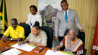 The Minister of Culture, Gender, Entertainment and Sport, the Honourable Olivia Grange (centre) and the Principal of Eckler Jamaica, Constance Hall (right) sign a contract towards establishing group health and life insurance scheme for entertainment, culture and creative industries practitioners in Jamaica.  Looking on is Permanent Secretary, Denzil Thorpe (left); Principal Director of Entertainment, Gillian McDaniel (2nd left); and Rohan Hall, Senior Consultant at Eckler Jamaica. 
