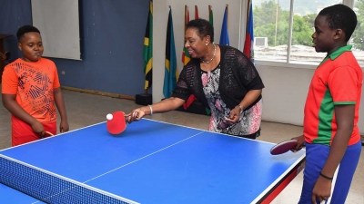 The Honourable Olivia Grange, Minister of Culture, Gender, Entertainment and Sport gets playing tips from Joel Butler (left) and Azizi Johnson, (right), under 13 and under 11 years players during a visit to one of their practice sessions on Tuesday at the Jamaica Theological Seminary in Kingston.
