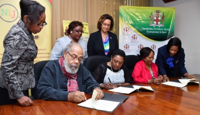 The Honourable Olivia Grange, Minister of Culture, Gender, Entertainment and Sport (centre) signs the Deed of Gift under which the Coverley Collection has been turned over to the National Library of Jamaica, an agency of the Ministry. The document was also signed by Fabian Coverley, son (second left) and Judge Pamela Appelt, Co-Executor, Louise Bennet Coverley Estate (second right), who is being assisted by Deon Ellignton, Team Leader, Advantage General Insurance Company Limited who signed as a witness (right). Looking on are: Georgette Grant, Legal Officer in the Ministry; Beverley Lashley, CEO, National Library of Jamaica and Marigold Harding, Deputy Chair, Institute of Jamaica (left to right).