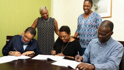 Minister of Culture, Gender, Entertainment and Sport, the Honourable Olivia Grange (centre) participates in signing of MOU between her Ministry and UN Women towards the implementation of the National Strategic Action Plan to Eliminate Gender-based Violence.  Also participating in the signing of the MOU are Representative of Multi-Country Office of the Caribbean Representative, Alison McLean (left) and Permanent Secretary in the Ministry, Denzil Thorpe (right).  Looking on are Marcia Ladine of UN Women (second left) and Sharon Robinson of the Bureau of Gender Affairs.